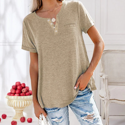 Femme en t-shirt beige avec boutons, jeans déchirés, posant près d'un vase de pommes rouges, intérieur lumineux. Mode décontractée, tendance.