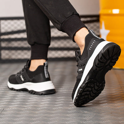 Chaussures de sport noires pour homme, semelle épaisse blanche, portées sur sol métallique. Confort, style urbain, mode masculine, baskets tendance.