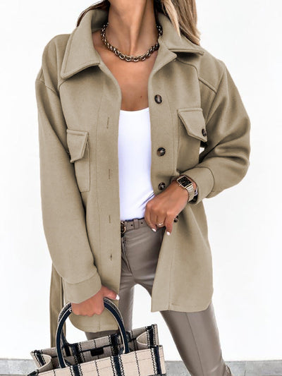 Femme portant une surchemise beige élégante avec boutons, t-shirt blanc, pantalon beige, collier doré, montre-bracelet, et sac à main à carreaux.