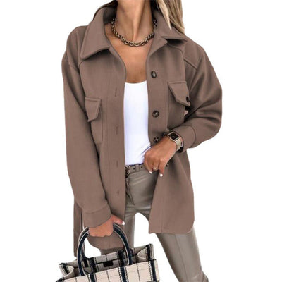 Femme portant une surchemise marron tendance, chemise blanche, pantalon beige, collier doré, tenant un sac à carreaux. Mode automne chic.