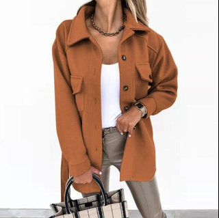 Femme portant une surchemise marron tendance, débardeur blanc, pantalon beige, avec un sac à main à carreaux. Mode automne chic et moderne.
