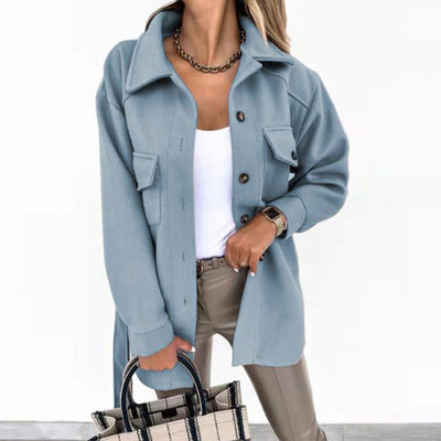 Femme portant une surchemise bleue élégante avec boutons, tenue chic avec pantalon beige et sac à main à carreaux, mode automne-hiver tendance.