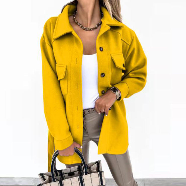 Femme portant une veste jaune tendance, chemise blanche et pantalon beige, tenant un sac à main à carreaux. Mode automne, style chic et moderne.