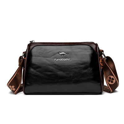Sac à bandoulière en cuir noir brillant avec logo kangourou, sangle marron à motifs floraux, design élégant et moderne pour femmes.