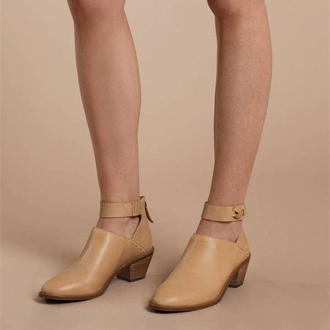 Chaussures en cuir beige à talons bas, avec bride cheville, portées par une personne sur fond beige. Mode élégante et tendance pour femmes.