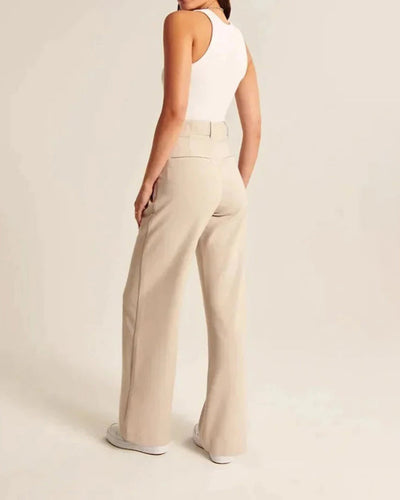 Femme en débardeur blanc et pantalon beige taille haute, vue de dos, style décontracté, mode féminine élégante, fond neutre.