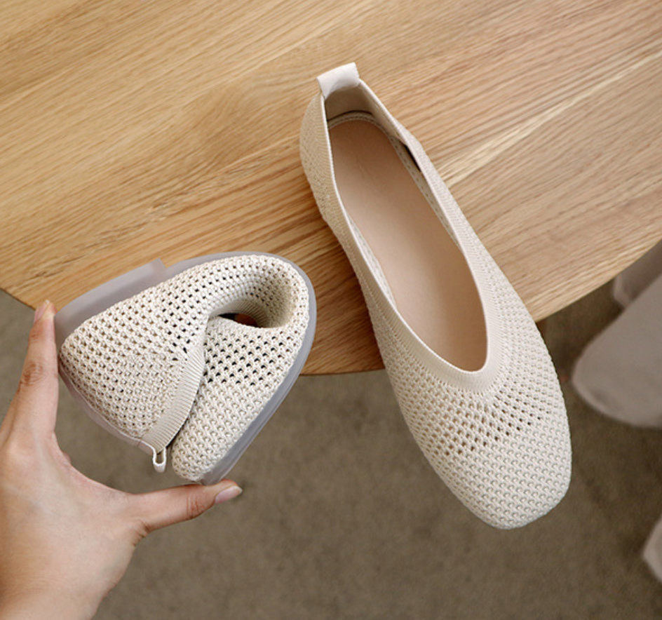 Ballerines pliables beiges en maille respirante sur une table en bois, design léger et confortable, idéales pour le voyage et le quotidien.