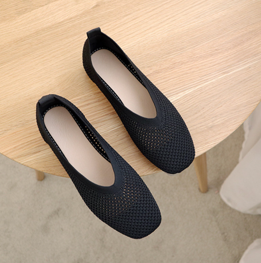 Ballerines noires en maille respirante sur une table en bois clair, chaussures élégantes et confortables pour femmes, mode décontractée.