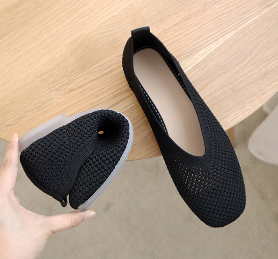 Chaussures pliables noires en maille sur une table en bois, design léger et respirant, idéales pour le voyage et le confort quotidien.