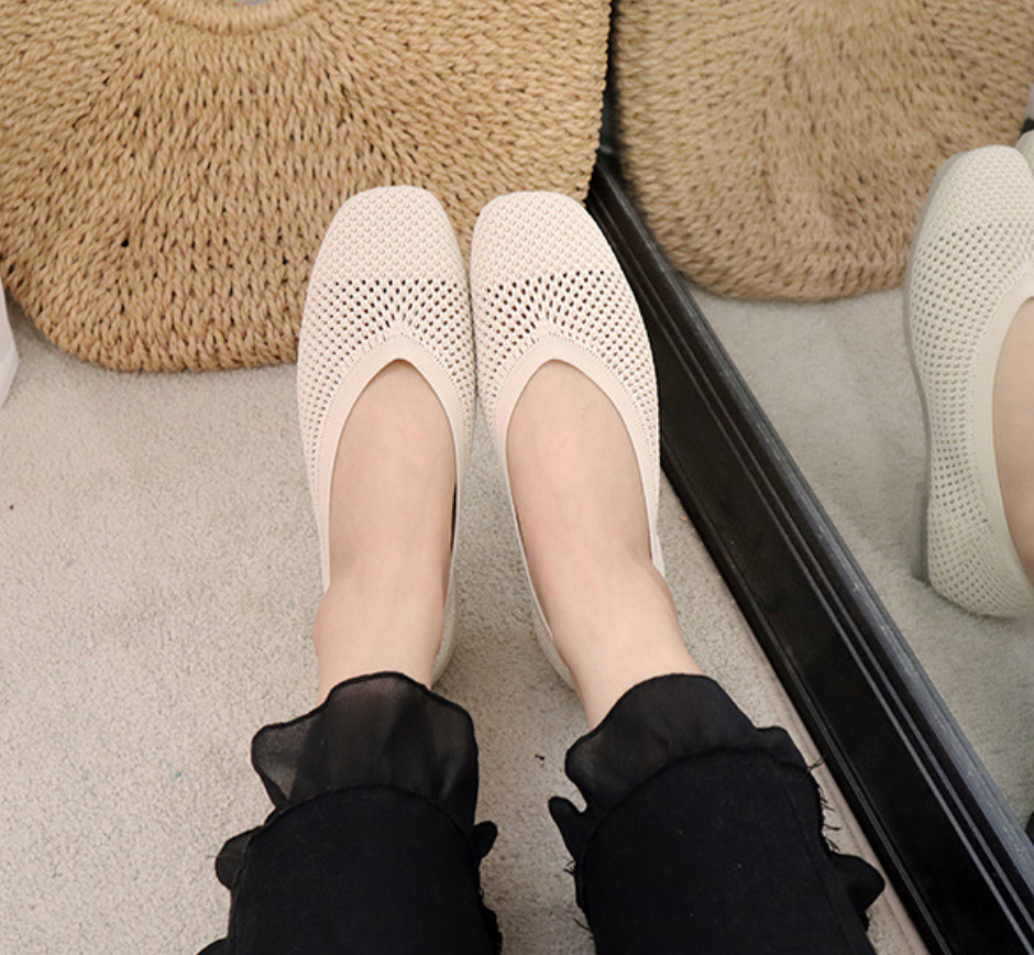 Chaussures plates blanches en maille respirante, portées avec un pantalon noir à volants, reflétées dans un miroir. Mode féminine élégante.