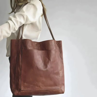 Sac en cuir marron porté par une femme, design minimaliste avec grande poche avant. Accessoire mode élégant et tendance pour femme.