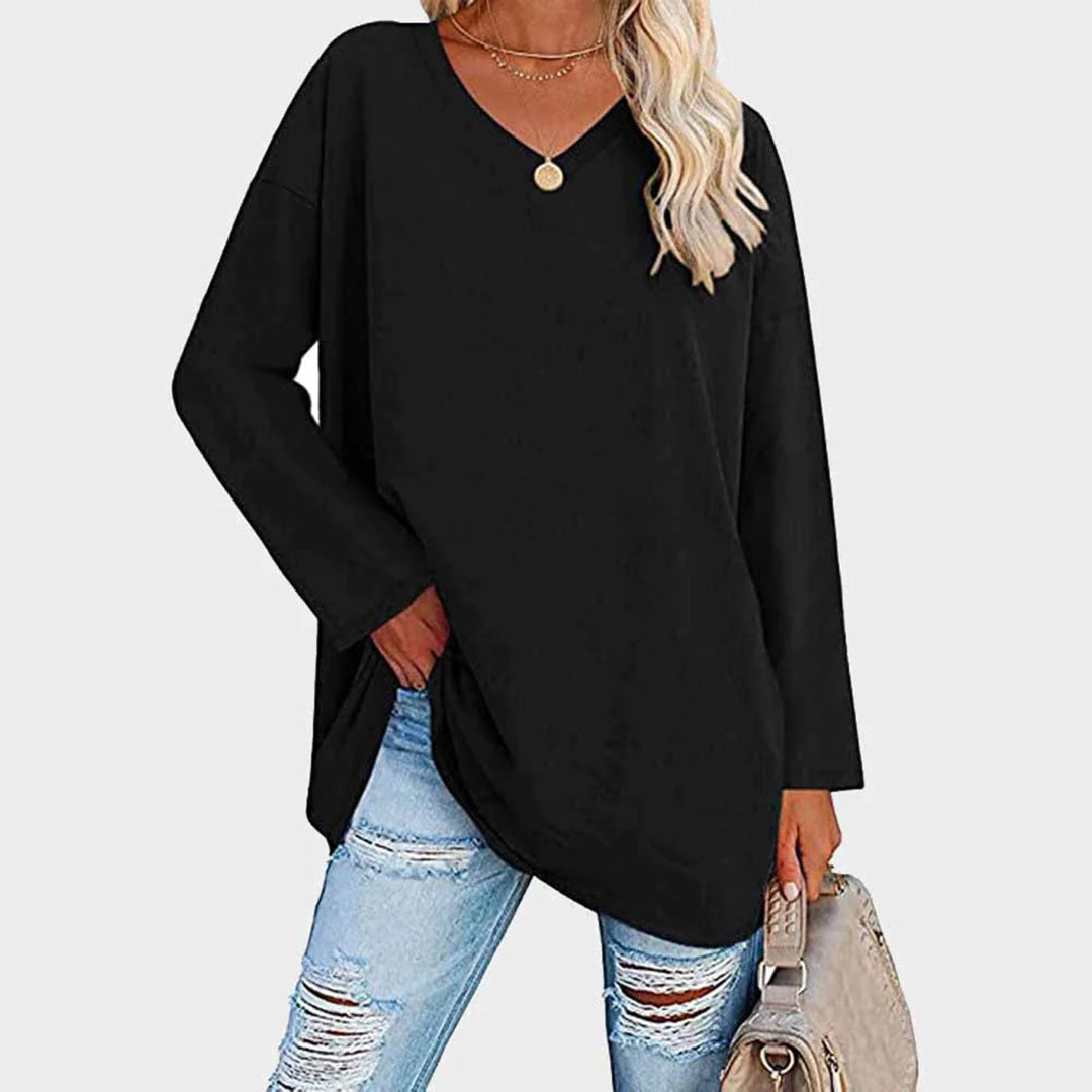 Femme portant un pull noir ample avec un collier doré, associée à un jean déchiré et un sac beige. Mode décontractée chic pour femme.