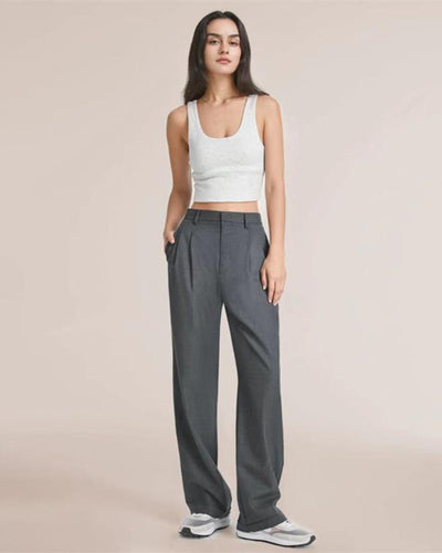 Femme en débardeur blanc et pantalon gris ample, posant debout. Mode décontractée, style minimaliste, tendance vêtements féminins.