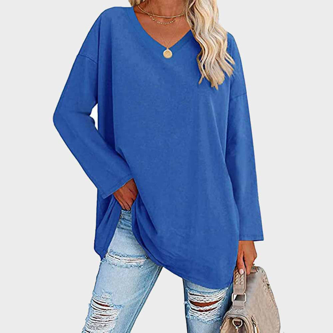 Femme portant un pull bleu ample à col en V, associé à un jean déchiré et un sac beige. Mode décontractée, tendance automne-hiver.