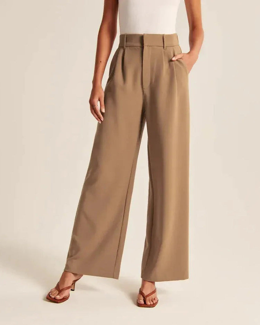 Pantalon large beige pour femme, taille haute, avec poches, porté avec un haut blanc sans manches et des sandales marron. Mode élégante et décontractée.