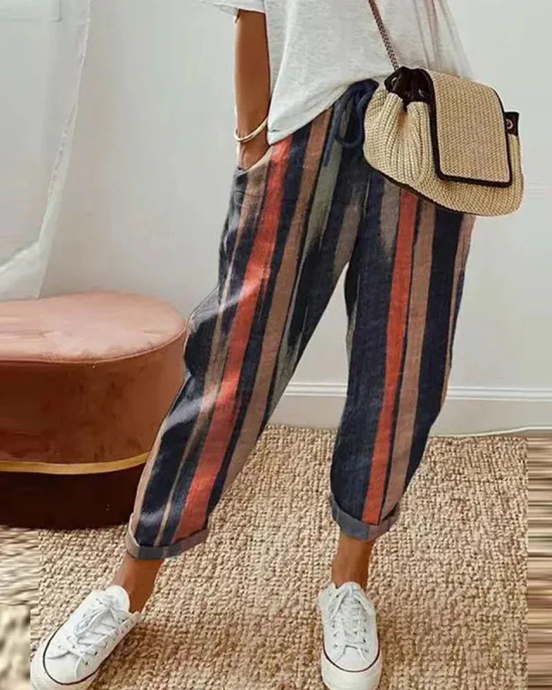 Pantalon rayé multicolore femme, style décontracté, avec sac en paille et baskets blanches. Mode tendance, tenue estivale chic et confortable.