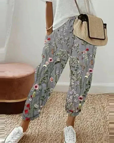 Pantalon femme à motifs floraux, porté avec un t-shirt blanc et un sac en paille. Style décontracté, tendance mode printemps-été.