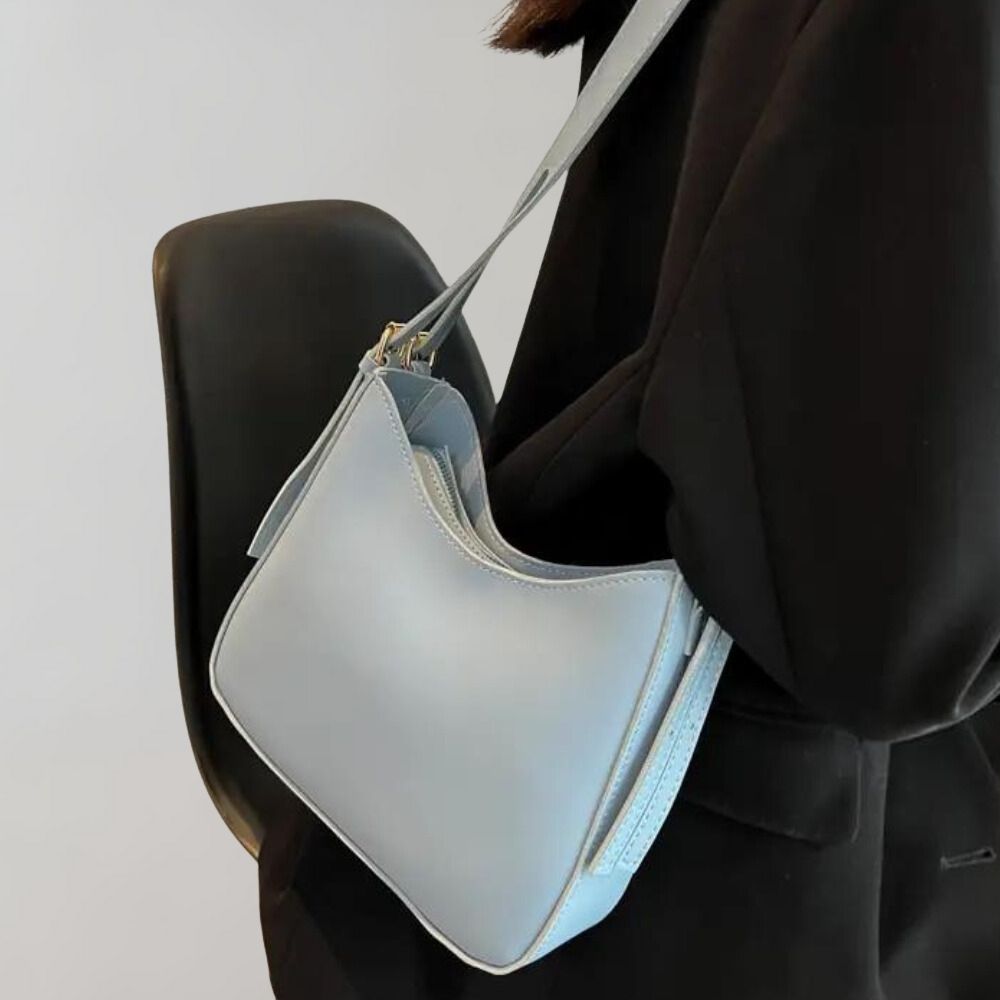 Sac à bandoulière bleu clair en cuir, porté par une personne en manteau noir. Accessoire mode élégant et tendance pour femmes.