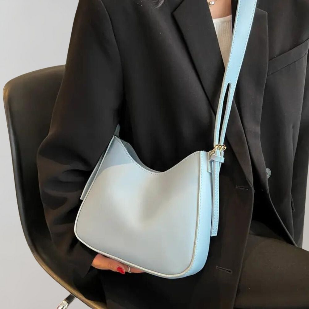 Sac à main bleu clair élégant porté par une personne en veste noire, assise sur une chaise. Accessoire mode tendance, design moderne et chic.