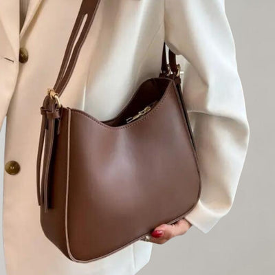 Sac à main marron élégant porté par une personne en veste blanche, design moderne, cuir lisse, idéal pour mode féminine et accessoires tendance.