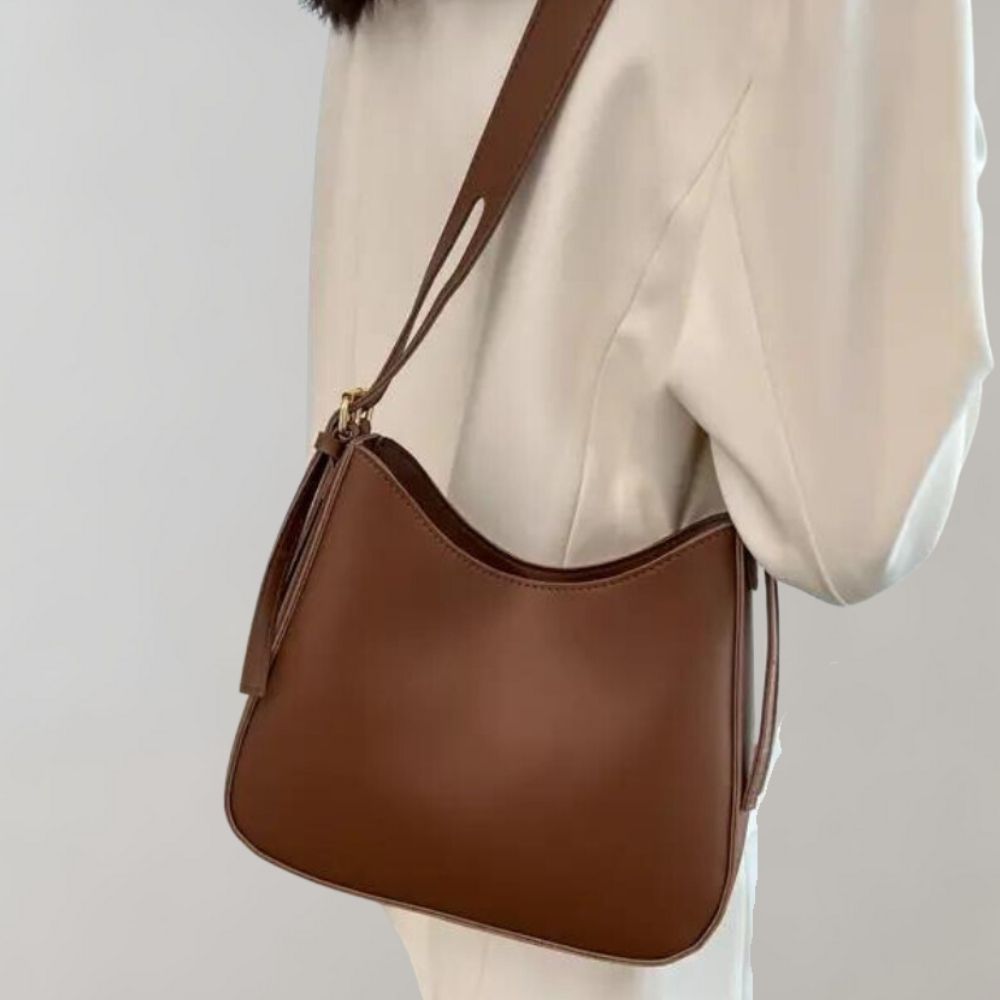 Sac à bandoulière en cuir marron porté par une personne en manteau blanc. Accessoire de mode élégant, tendance, idéal pour un look chic et moderne.