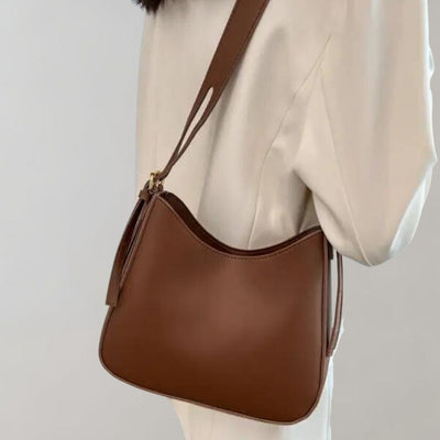 Sac à bandoulière en cuir marron porté par une personne en manteau blanc. Accessoire de mode élégant, tendance, idéal pour un look chic et moderne.