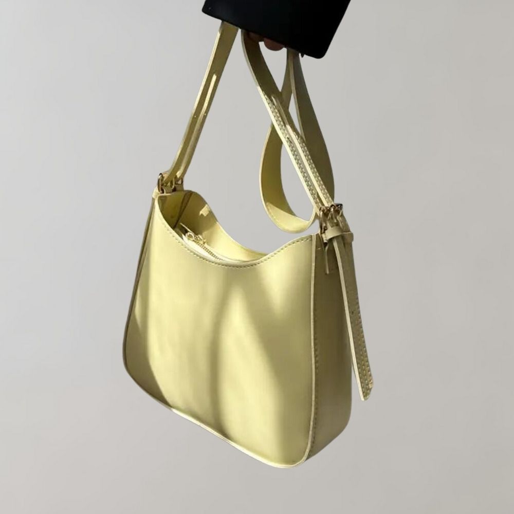 Sac à main en cuir jaune pâle, design minimaliste, bandoulière ajustable, fond gris clair. Accessoire mode élégant et tendance pour femmes.