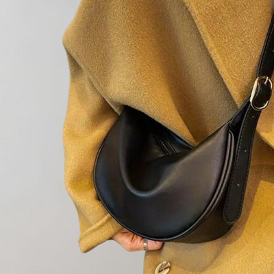 Sac à main en cuir noir élégant porté sur un manteau beige, design moderne et minimaliste, accessoire de mode tendance pour femmes.
