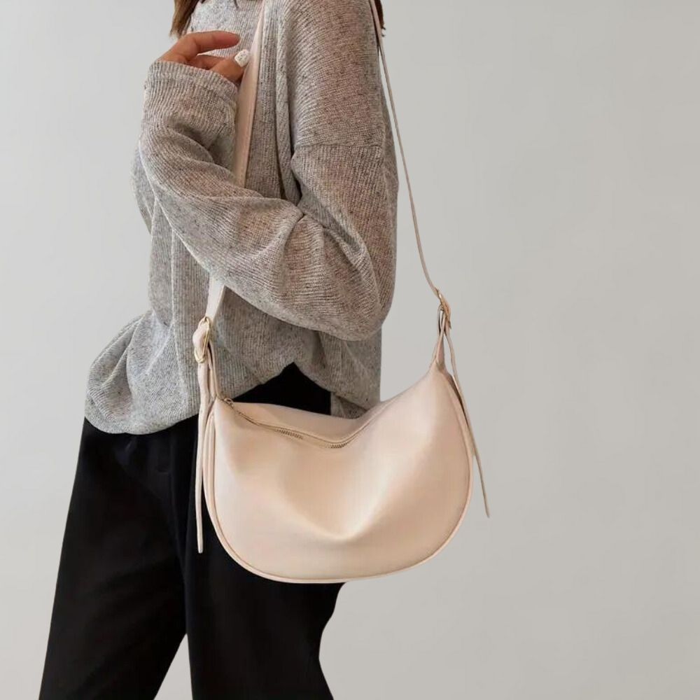 Femme portant un pull gris et un sac à bandoulière beige élégant. Mode automne, style décontracté, accessoires tendance.