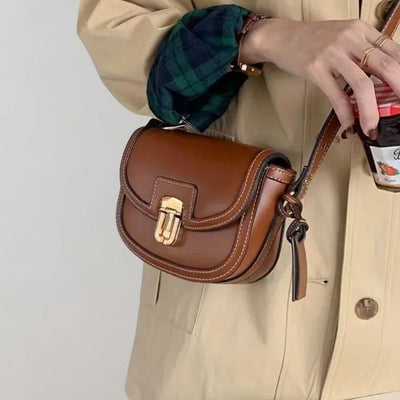 Sac à main en cuir marron avec boucle dorée, porté par une personne en manteau beige. Accessoire mode élégant et tendance.