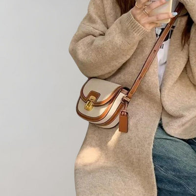 Sac à bandoulière beige et marron en cuir, porté par une femme en manteau beige, tenant une boisson. Mode automne, accessoire tendance.