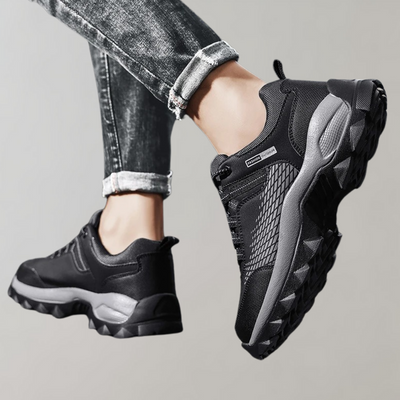 Chaussures de sport noires pour homme, semelle épaisse antidérapante, portées avec un jean. Idéales pour la randonnée et le plein air.