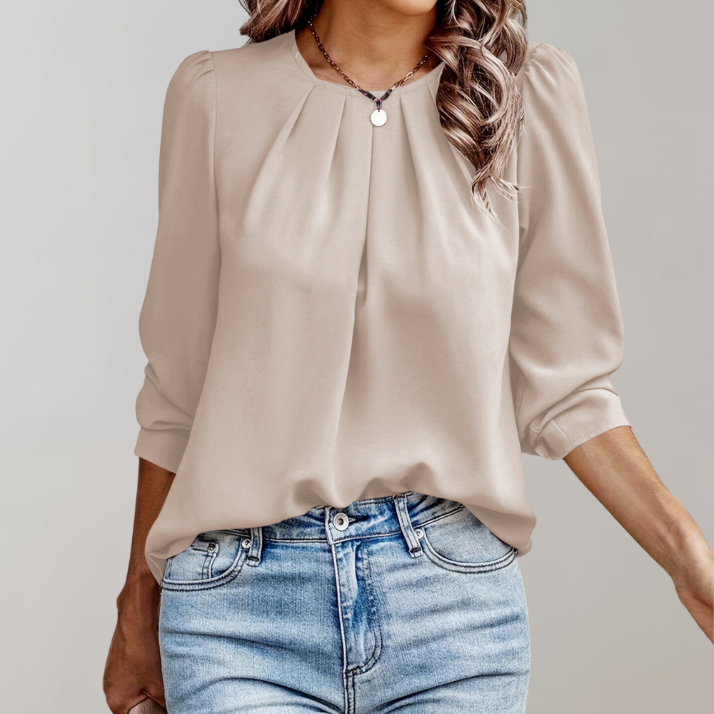 Blouse beige élégante avec manches longues, col plissé, portée avec un jean bleu clair. Mode féminine chic et décontractée.