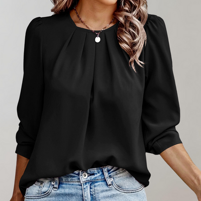 Femme portant un chemisier noir élégant avec manches longues et col plissé, associé à un jean bleu décontracté. Mode féminine chic et moderne.