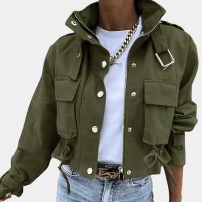 Veste militaire verte pour femme avec poches, boutons argentés et ceinture, portée sur un t-shirt blanc et un jean. Mode automne tendance.