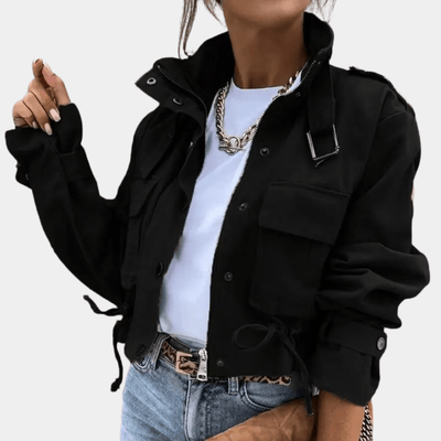 Veste noire femme tendance, manches longues, poches avant, portée avec t-shirt blanc, jean bleu et collier chaîne doré. Mode automne chic.