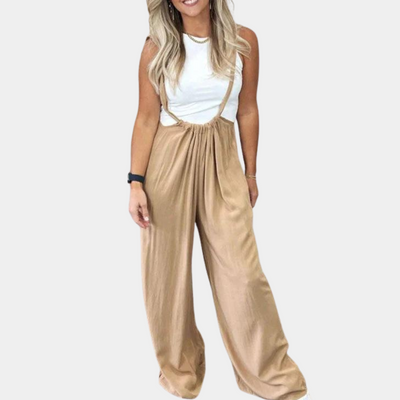 Femme portant une salopette beige ample avec un haut blanc sans manches. Mode décontractée, tendance, élégante. Accessoires: montre noire, collier.