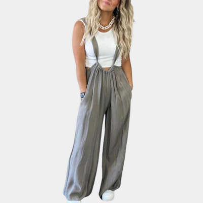 Femme portant une salopette ample grise avec un débardeur blanc et des baskets blanches. Mode décontractée, tendance, style urbain.