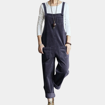 Salopette en velours côtelé bleu marine pour femme, avec poches avant, portée sur un t-shirt blanc à manches longues. Mode décontractée élégante.