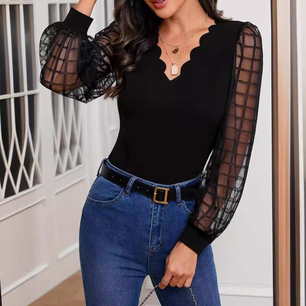 Femme portant un haut noir élégant avec manches en tulle transparent et un jean bleu, posant dans un intérieur moderne. Mode féminine chic.