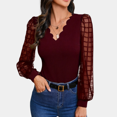 Femme portant un haut bordeaux à manches longues transparentes et col en V festonné, associé à un jean bleu et une ceinture noire.