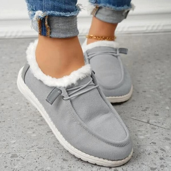Chaussures mocassins gris pour femme avec doublure en fausse fourrure blanche, portées avec un jean retroussé. Confortables et tendance.