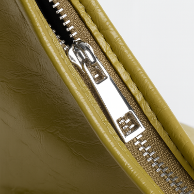 Gros plan sur une fermeture éclair métallique argentée sur un sac en cuir vert olive, texture détaillée, mode accessoires, design moderne.