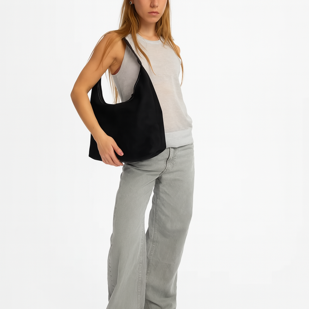 Jeune femme portant un sac à main noir moderne, vêtue d'un débardeur blanc et d'un jean gris. Mode féminine, accessoires tendance.