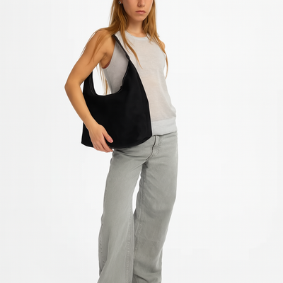 Jeune femme portant un sac à main noir moderne, vêtue d'un débardeur blanc et d'un jean gris. Mode féminine, accessoires tendance.