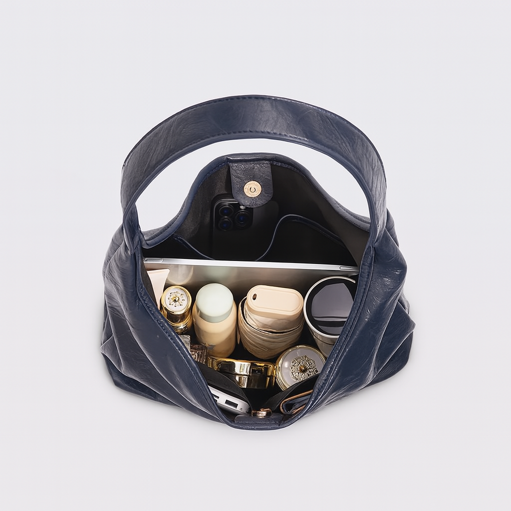 Sac à main en cuir bleu ouvert, contenant un smartphone, tablette, produits de beauté et accessoires. Organisation pratique et élégante.