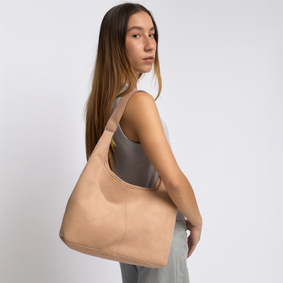 Femme portant un sac à main beige en cuir, style épaule, sur fond blanc. Mode féminine, accessoire tendance, élégance moderne.