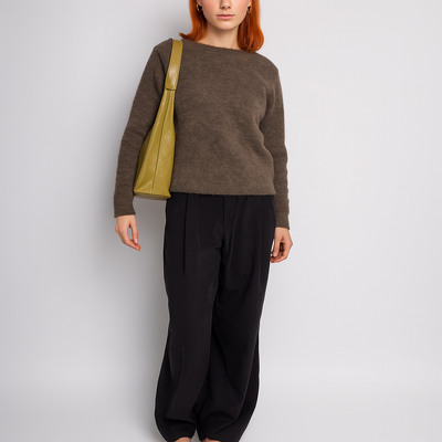 Femme aux cheveux roux portant un pull marron, pantalon noir ample et sac à main vert olive. Mode automne, style décontracté élégant.