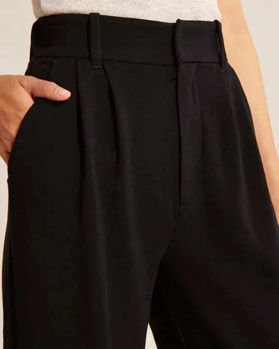 Pantalon noir taille haute pour femme avec plis, ceinture à passants, main dans la poche, style élégant et moderne, mode féminine chic.