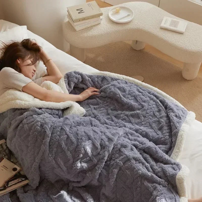 Femme dormant sous une couverture en fausse fourrure grise sur un lit, livres à côté, intérieur moderne, ambiance cosy et relaxante.